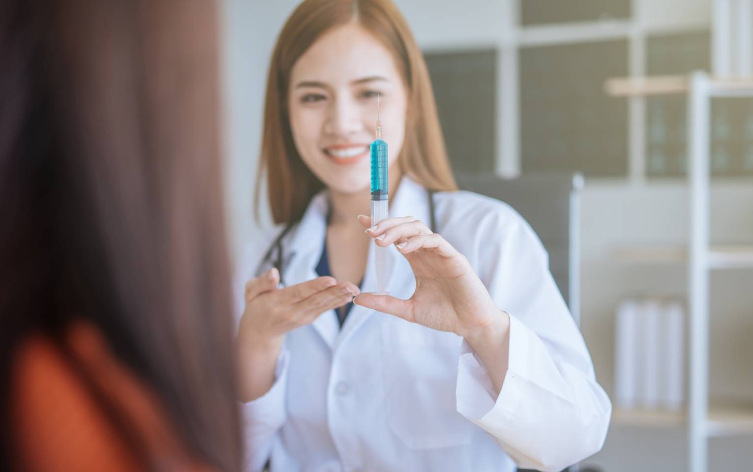 Female pharmacist showing a vaccine syringe to a patient